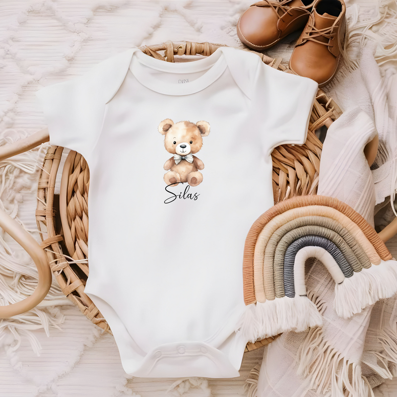 Kleines Bügelbild eines braunen Teddybären mit blauer Schleife, personalisiert mit Namen in schwarzer Schrift. Ideal für Babykleidung, Decken oder individuelle Geschenke.