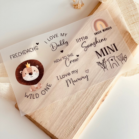 Bügelbild-Set mit Baby-Sprüchen wie "Wild One", "I Love My Daddy" und "New to the Crew" sowie Löwen-Motiv