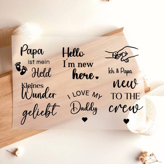 Bügelbild-Set mit Baby-Sprüchen wie "Hello I'm New Here", "Kleines Wunder" und "Papa ist mein Held" in Schwarz