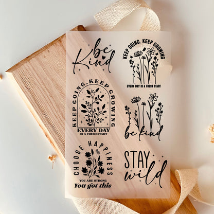 Bügelbild-Set mit floralen Strichzeichnungen und Sprüchen wie "Be Kind", "Stay Wild" und "Keep Going, Keep Growing" in Schwarz